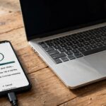 Phone showing WhatsApp chat backup progress beside a laptop